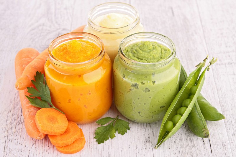 Baby Food Subscription Box - Three jars of natural homemade food, carrot, pea, and pear. Fresh carrots, peas, and parsley sitting along side