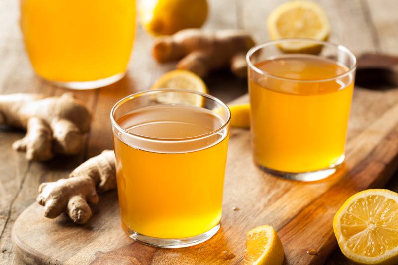 Three glases of kombucha on a table, with ginger and lemon