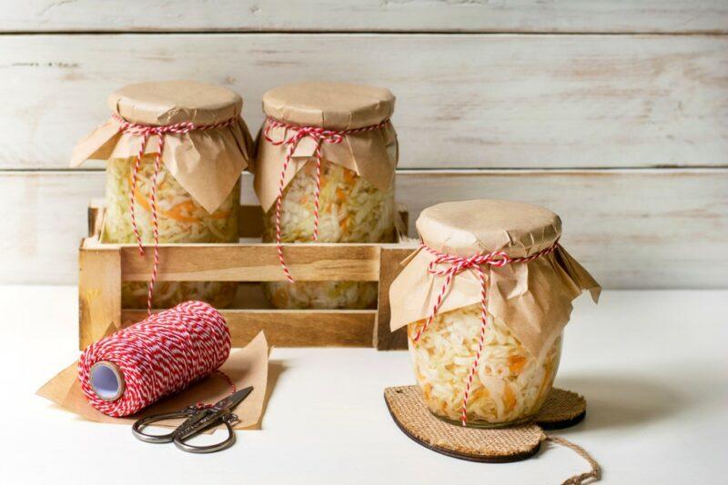 Three jars of sauerkraut with paper on top, next to some pink twine