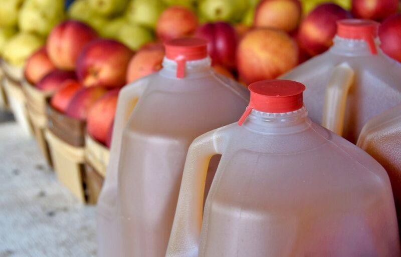 Four large bottles of apple cider, in front of crates of apples