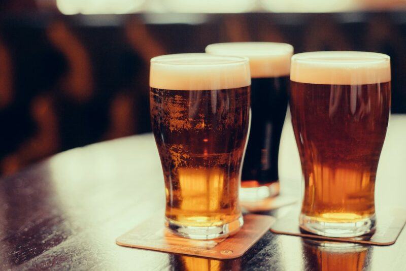 Three large glasses of beer on a table with coasters. Two beers are lighter than the other.