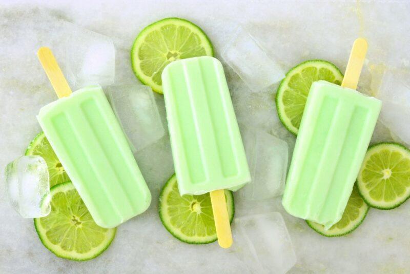 Three lime popsicles with slices of lime underneath them