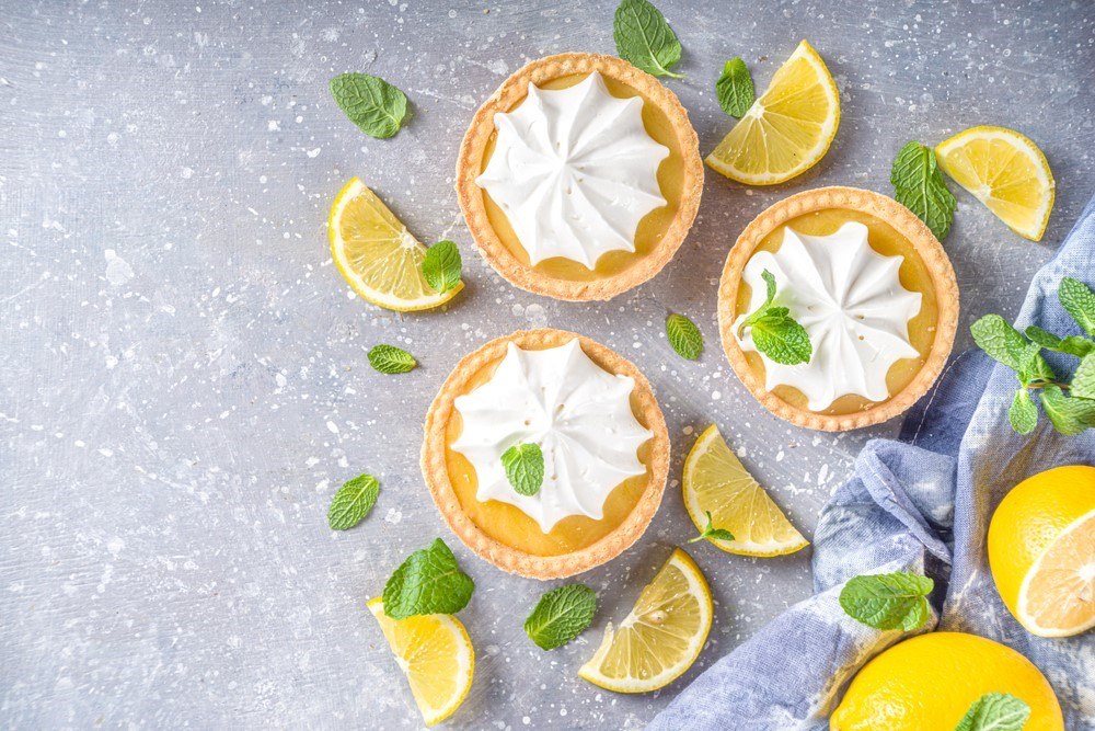 Three lemon tarts with a meringue topping, next to lemon wedges and leaves