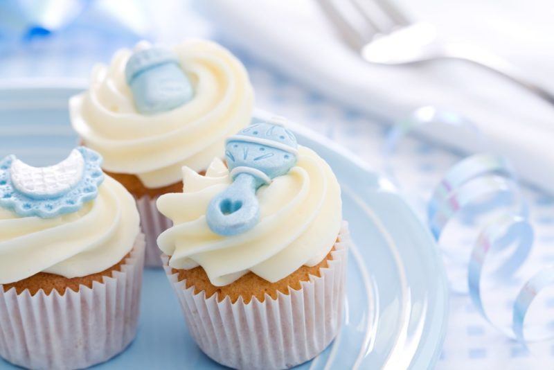 A light blue plate with three muffins that have white icing and blue baby shower decorations