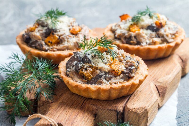 Three tarts containing mushroom and pumpkin, topped with herbs