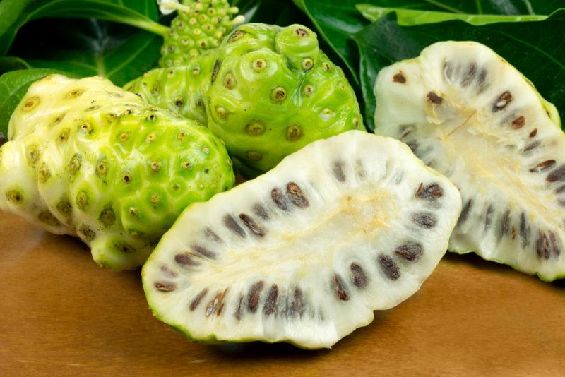 Three noni fruit, one of which has been sliced in half