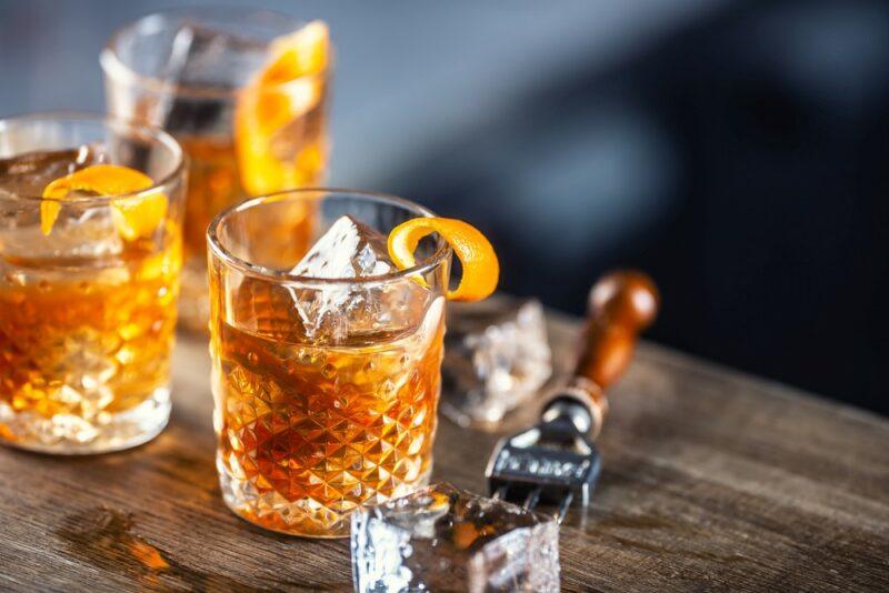 Three old fashioned cocktails on a bar, next to ice and an ice shaver