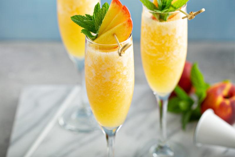 Three peach cocktails that are garnished with peaches and mint