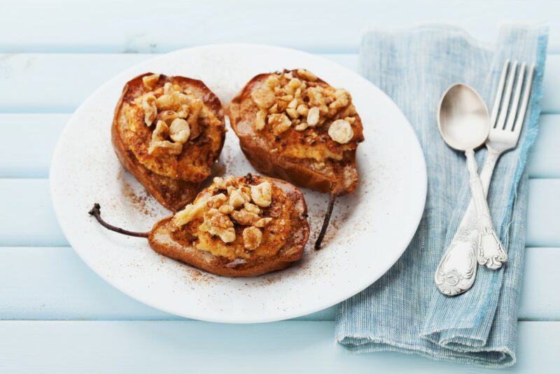 A white dish with three cooked pear halves, all of which have been stuffed with walnuts