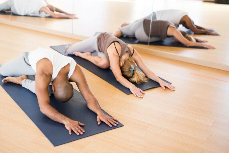 Three people practicing yoga in a studio, with their reflections visible in the mirror