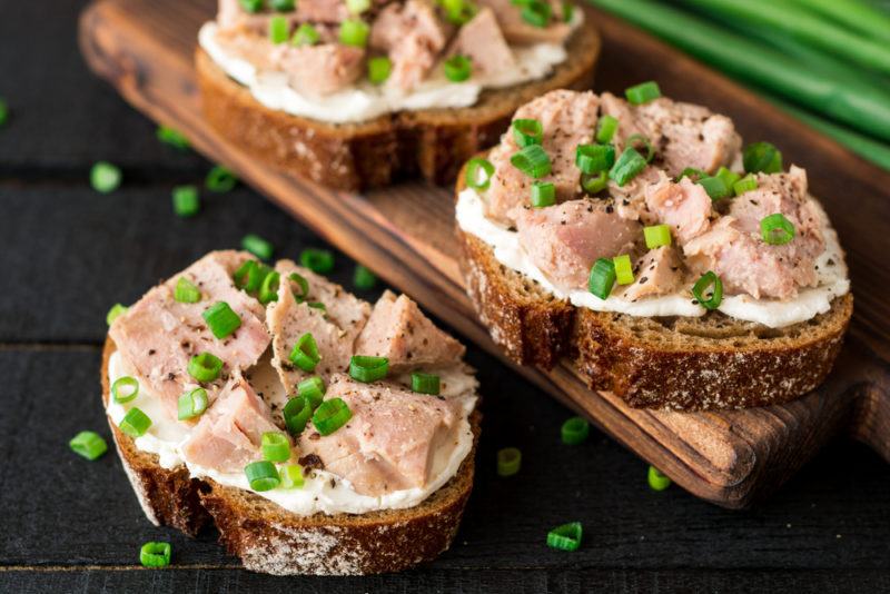 Three slices of bread with a white spread, tuna from a can and chives