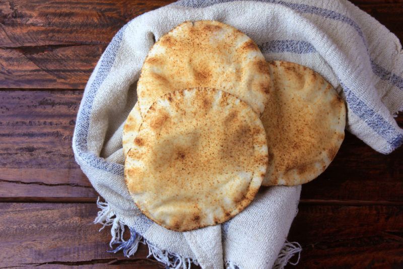 A wooden table with a cloth and three pieces of pita bread