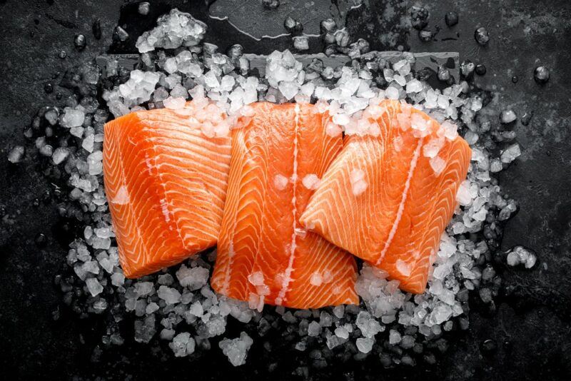 Three pieces of raw salmon on a black table with ice