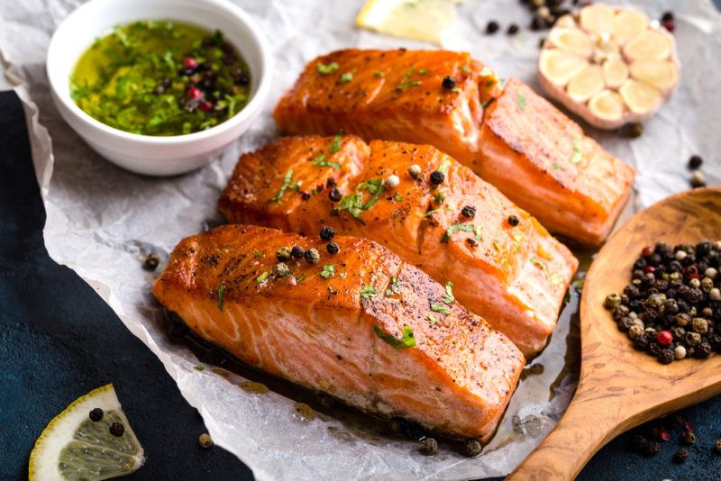 Three pieces of salmon sliced on a piece of parchment paper, with pesto and garlic