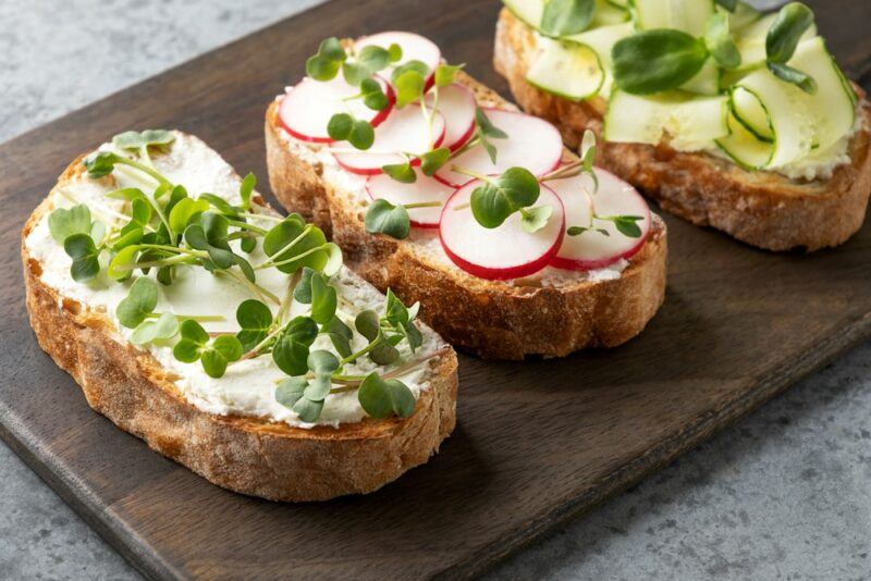 Three slices of sourdough, each with cream cheese and some fresh vegetables on top