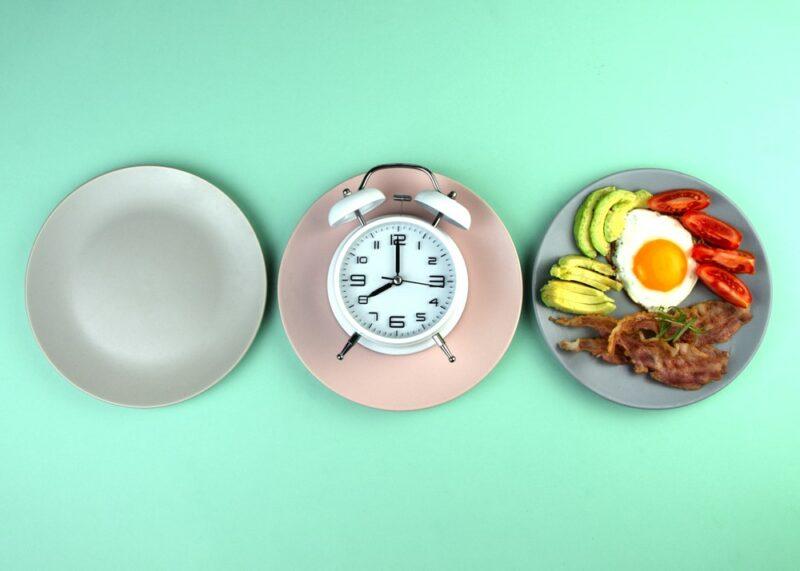 Three plates on a light blue table, one empty, one with a clock, one with food