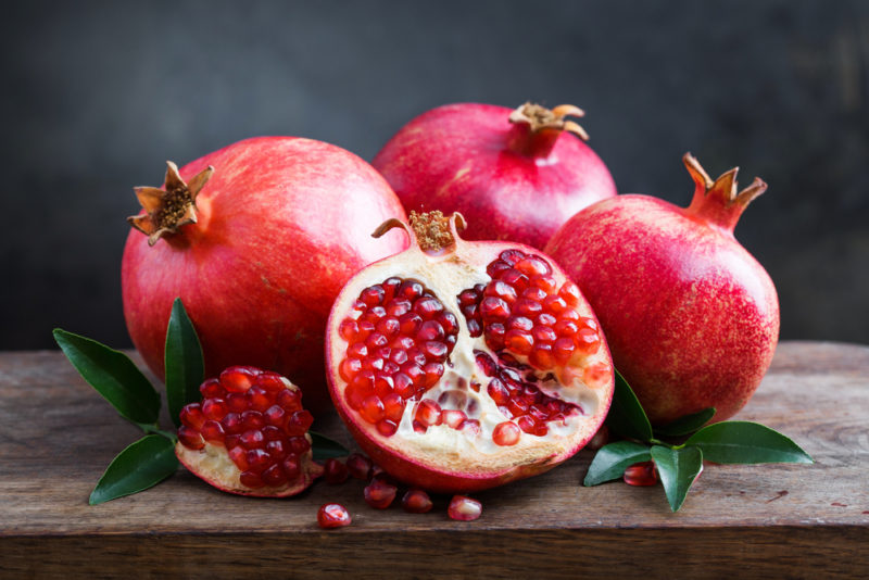 Three pomegranates with a fourth pomegranate that has been sliced open on a wooden board or table