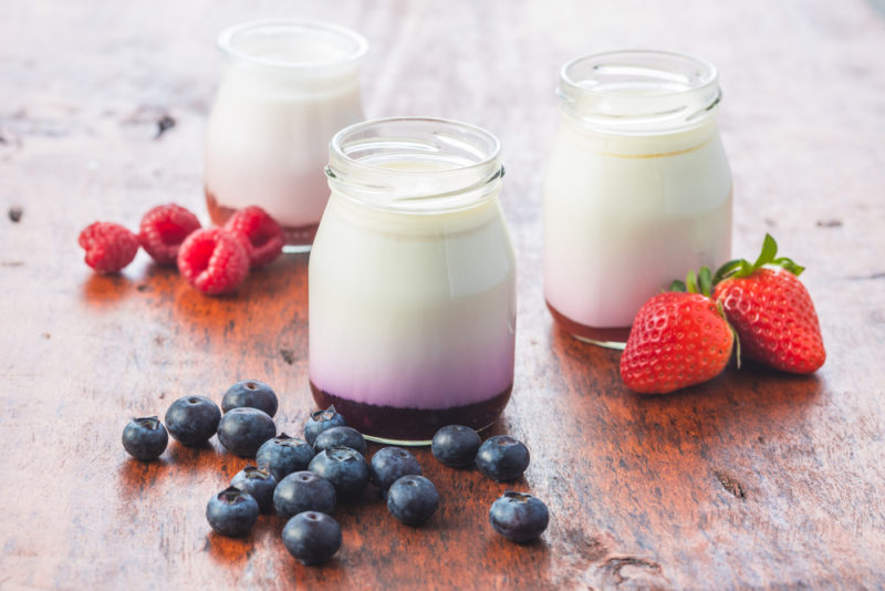 Three glass jars of yogurt with fruit at the bottom and fruit on the table