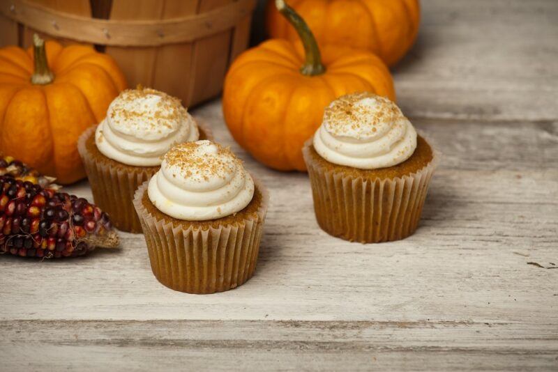 A wooden table with three pumpkin cream cheese muffins with cream cheese frosting, plus some pumpkins in the background