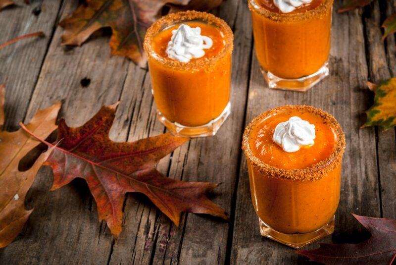 Three glasses of pumpkin pie shots on a wooden table with autumn leaves