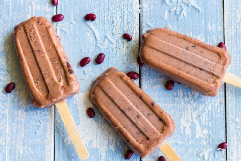 A light blue table with three red bean popsicles, plus some red beans