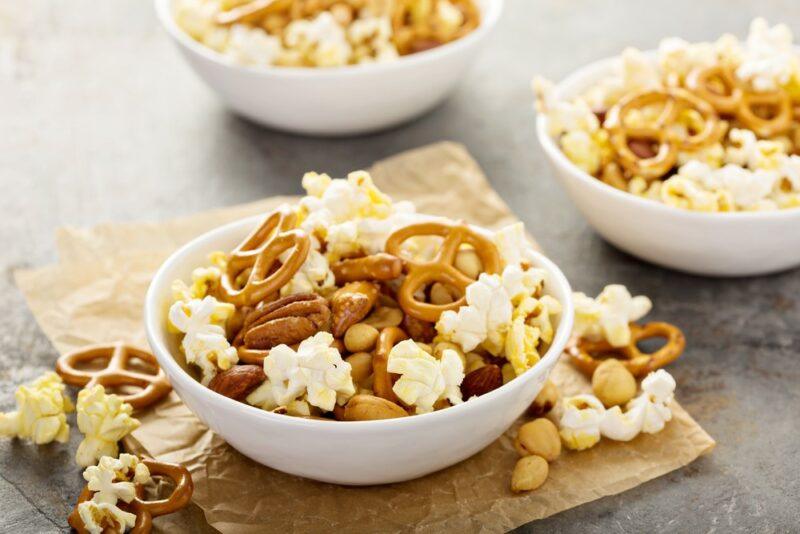 Three white dishes of trail mix containing popcorn, pretzels, and nuts