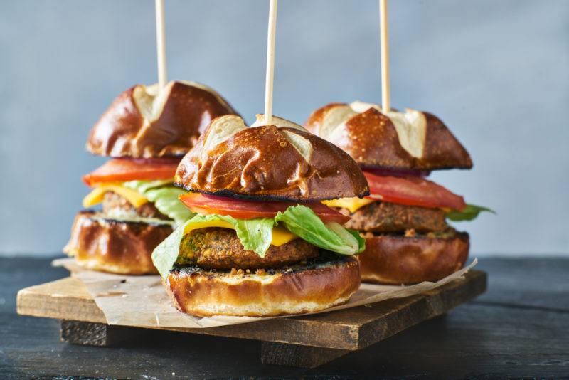 A wooden board with three small burgers with a vegan meat alternative and a skewer stuck through them