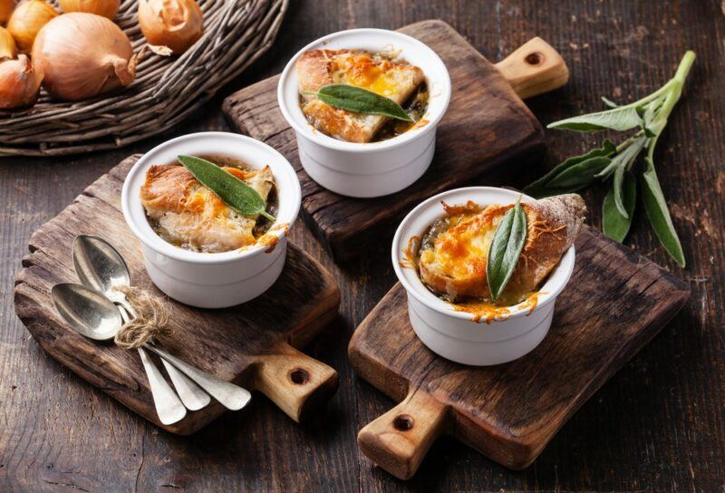 Three small containers of French onion soup on wooden boards