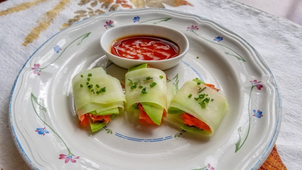 A white plate with three rolls that use cucumbers as the wrap material