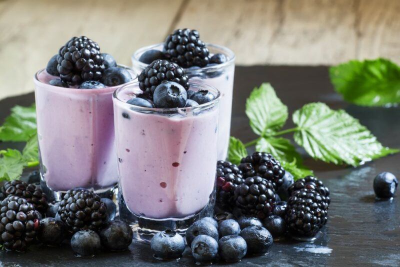 Three glasses containing a blackberry smoothie, with blackberries on the top