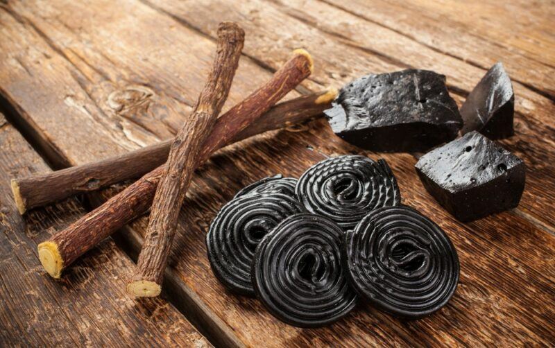 A wooden table or deck with pieces of licorice, some licorice rounds, and licorice roots