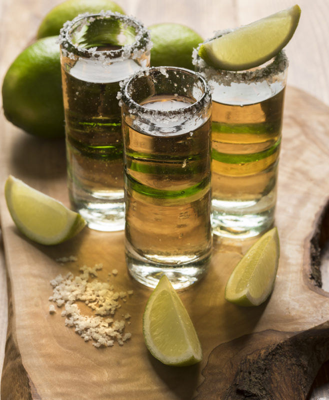 Three tequila slammers on a wooden board with salt and lime chunks