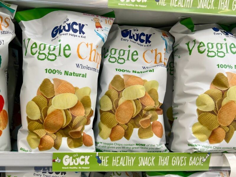 A grocery store shelf with green labels and bags of white veggie chips