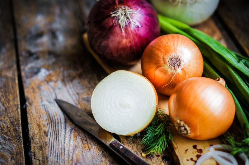 Two white onions, one red onion and haldf a white onion next to a knife