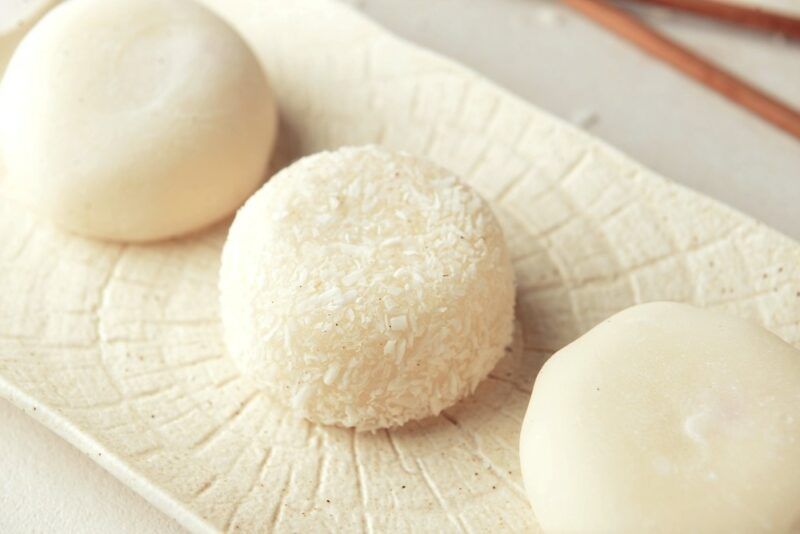 A white dish with three white pieces of nuomici. The middle one is topped with coconut