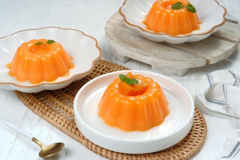 Three white plates containing formed Chinese mango puddings each topped with a leaf