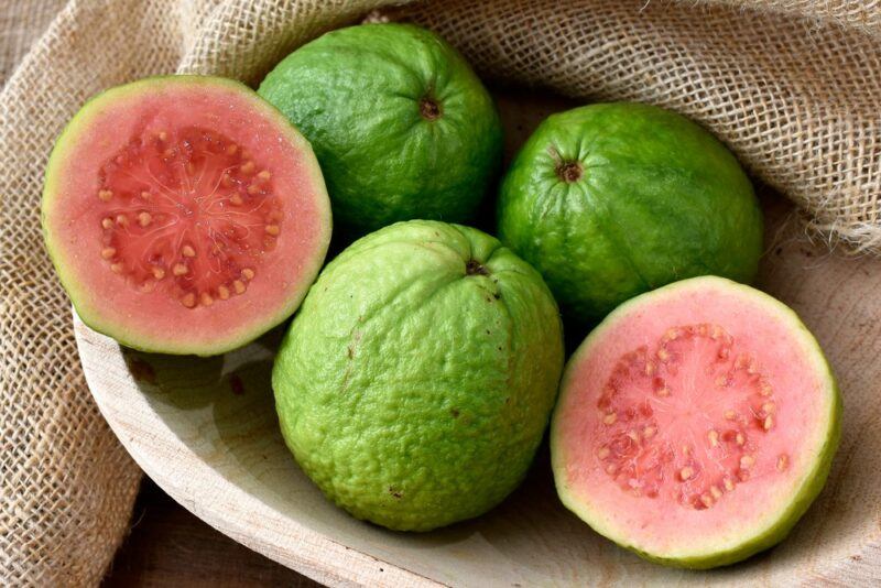 A bowl with a piece of cloth that contains three whole guavas and two guava halves