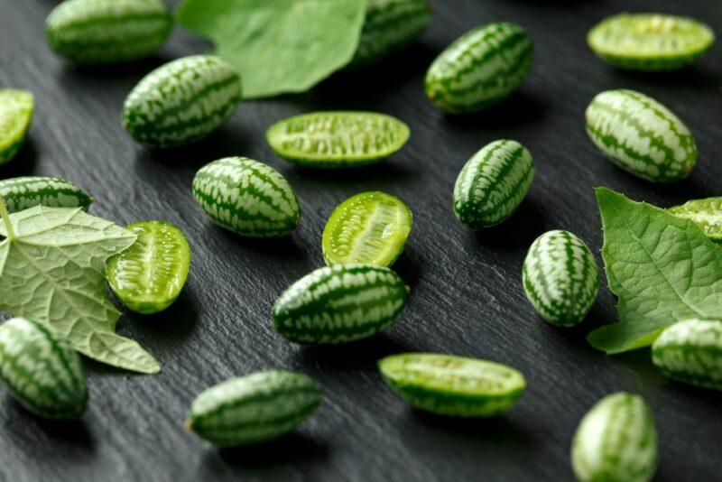 Various small cucamelons scattered on a black table. Some are whole, others have been cut in half