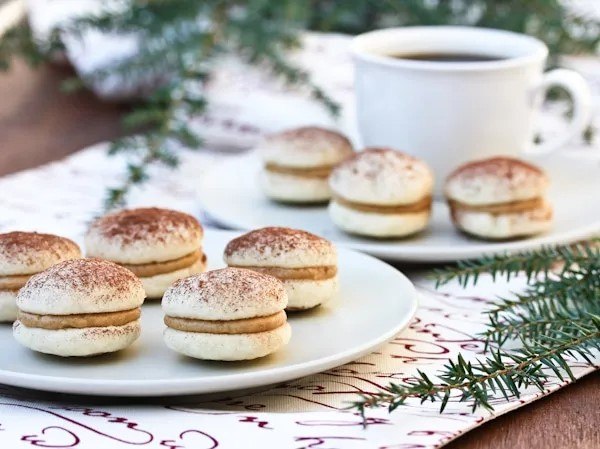 Two white plates with a selection of tiramisu cookies with filling, plus a cup of coffee