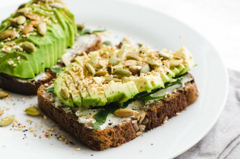 A white plate with two slices of toast, with avocado, and pumpkin seeds