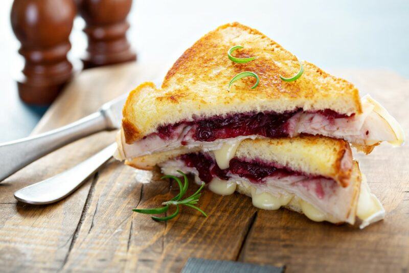 A turkey, cheese, and cranberry toasty that has been cut in half on a wooden board