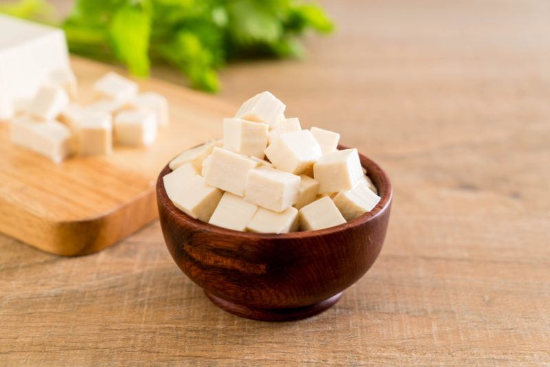 A wooden bown with tofu chunks and more chunks on a wooden board