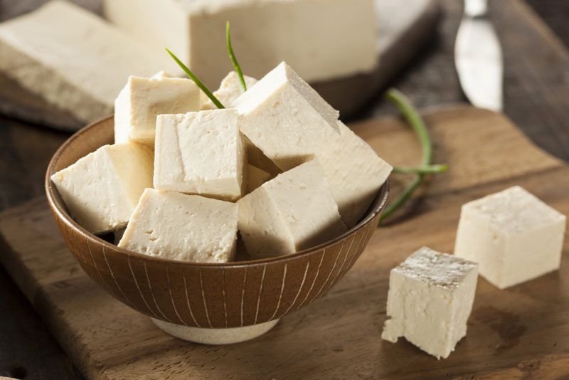 A bown containing chopped up tofu on a cutting board