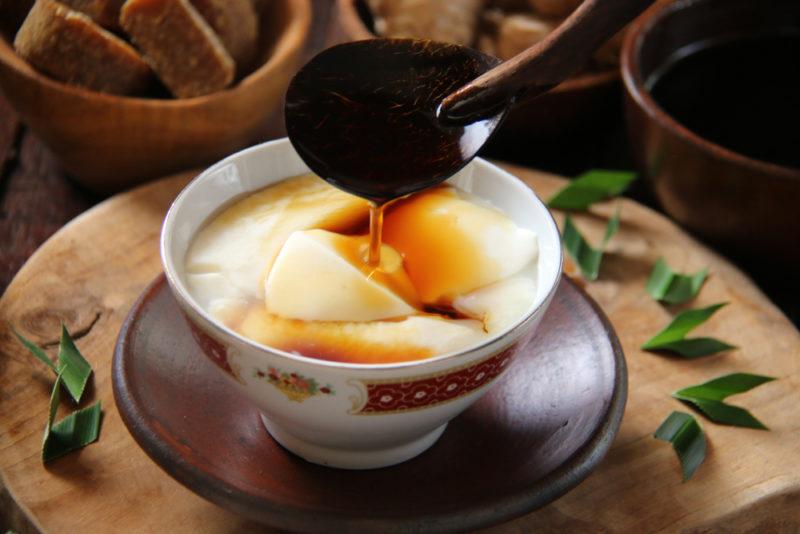 A white dish of tofu pudding with brown sugar syrup or soy sauce being ladled in