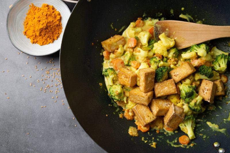 A tofu stir fry in a wok next to turmeric