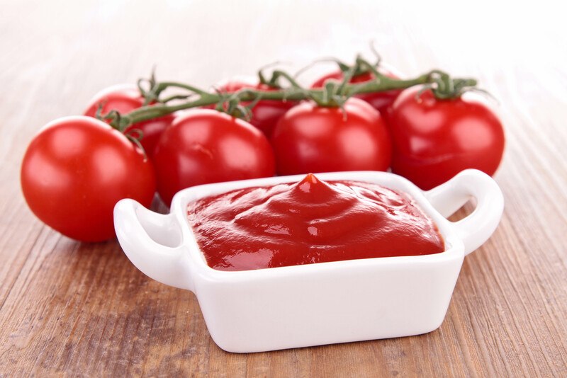 Several tomatoes and a white dish filled with tomato sauce rest on a wooden tabletop.