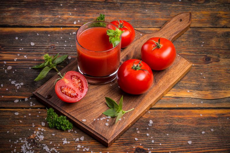 A glass of tomato juice with two tomatoes and a sliced tomato