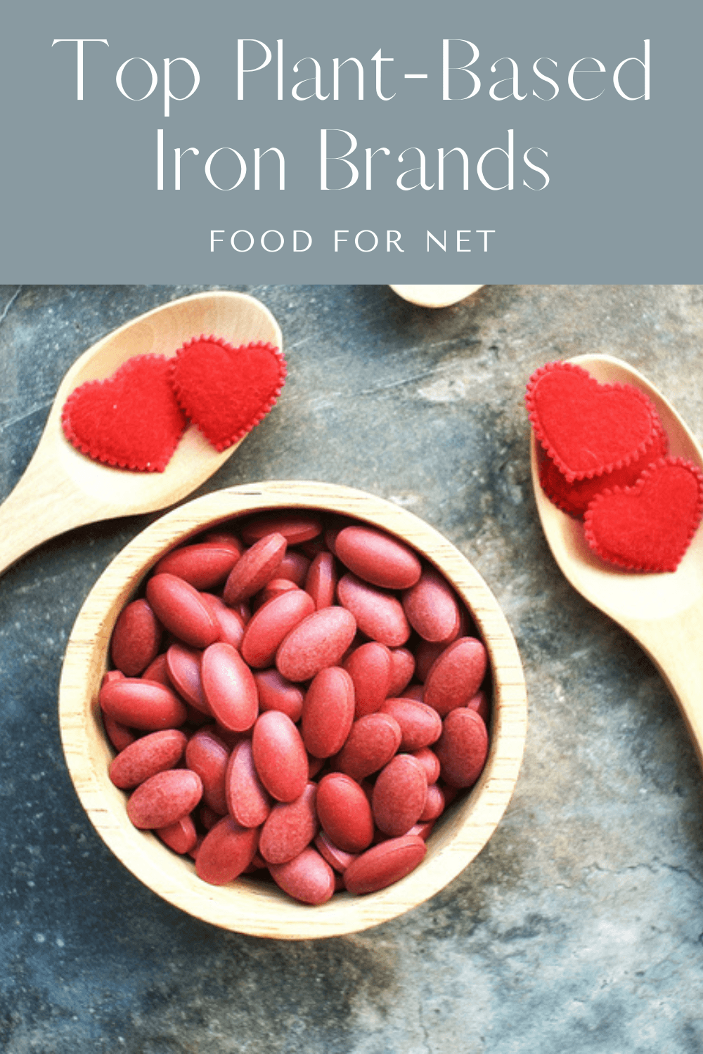 A brown bowl of red iron supplements, next to spoons with hearts