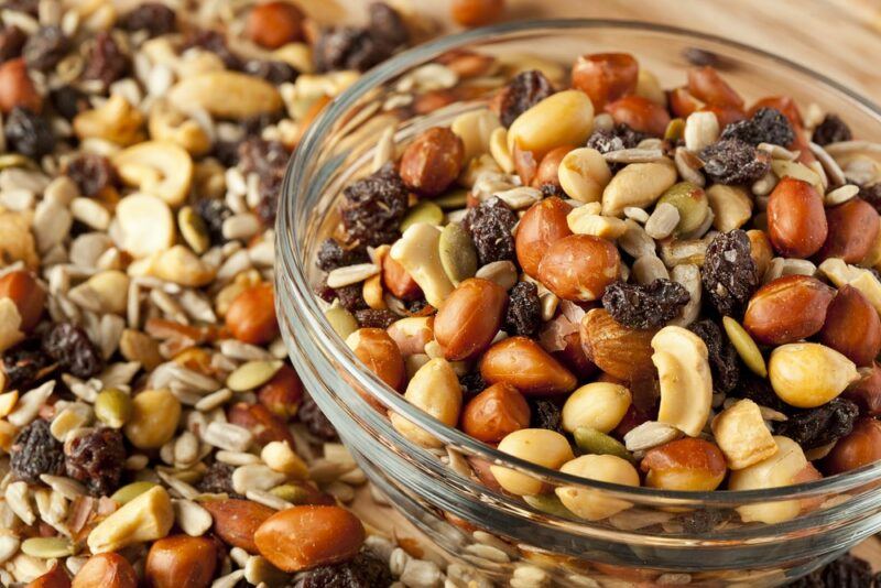 A pile of trail mix on a wooden table, next to a glass dish of trail mix