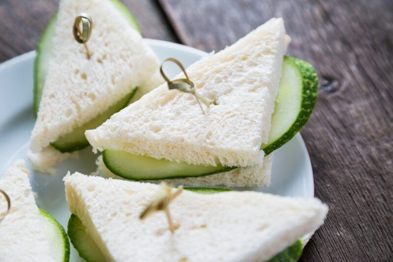 A white plate containing cucumber sandwiches cut into triangles with cocktail sticks through them